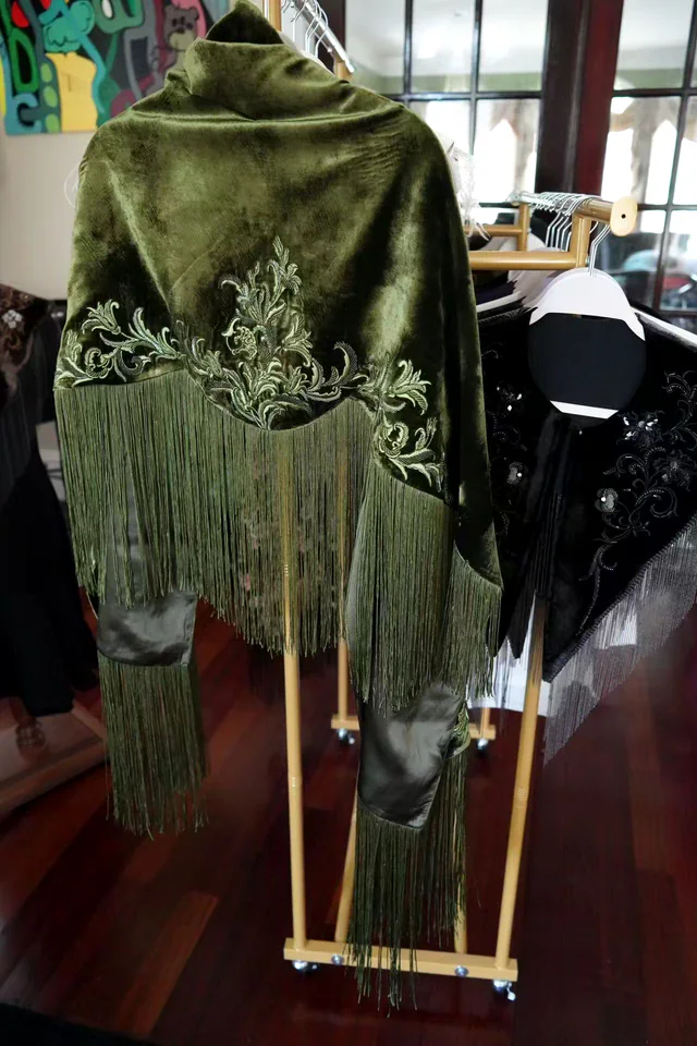 Olive velvet embroidered fringe shawl displayed on a garment rack